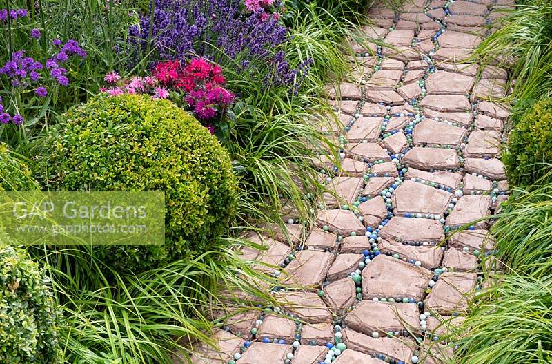 Pathway leading past border with clipped topiary balls and ornamental grasses. The Very Hungry Caterpillar Garden, RHS Tatton Park Flower Show, 2019.
