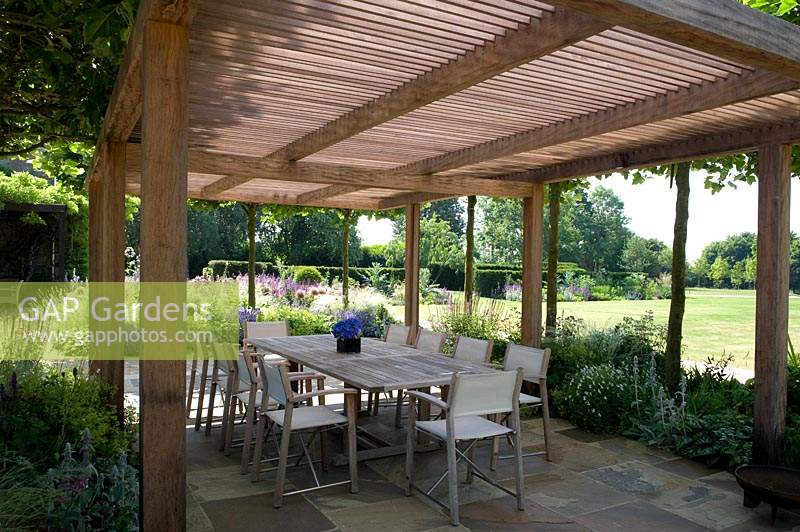 Wooden pergola shading dining area with table and chairs. 