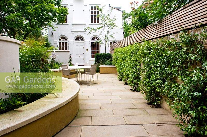 View of paved, urban garden, with dining area and formal planting. 