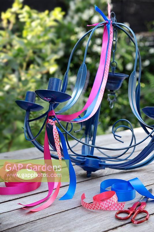 Cut lengths of brightly coloured ribbon and fasten on to the top of the sprayed chandelier, allowing the ribbon to drape. Leave a length once the ribbon is secured at the bottom so this will flutter in the breeze