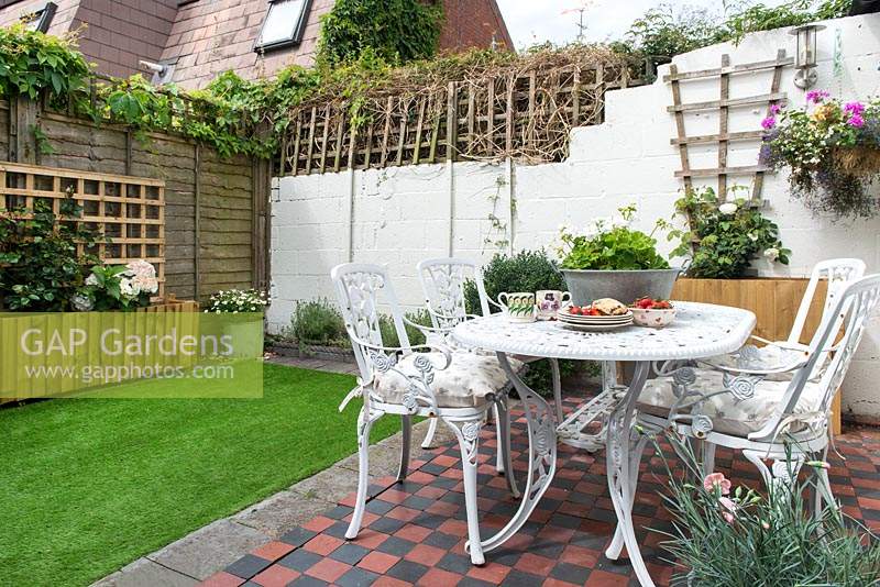 Tiny courtyard garden with tiled area, metal furniture, raised beds and artificial grass