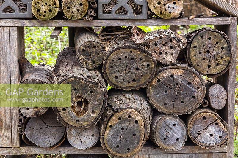 Bug hotel made from cut logs with drilled holes for insects plus straw and twigs