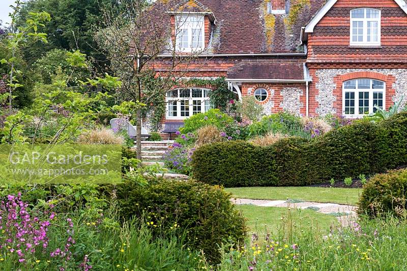 View over wildflowers, fruit trees and lawn enclosed in yew hedges to upper terrace below  flint and brick cottage, originally a farm labourer's dwelling.