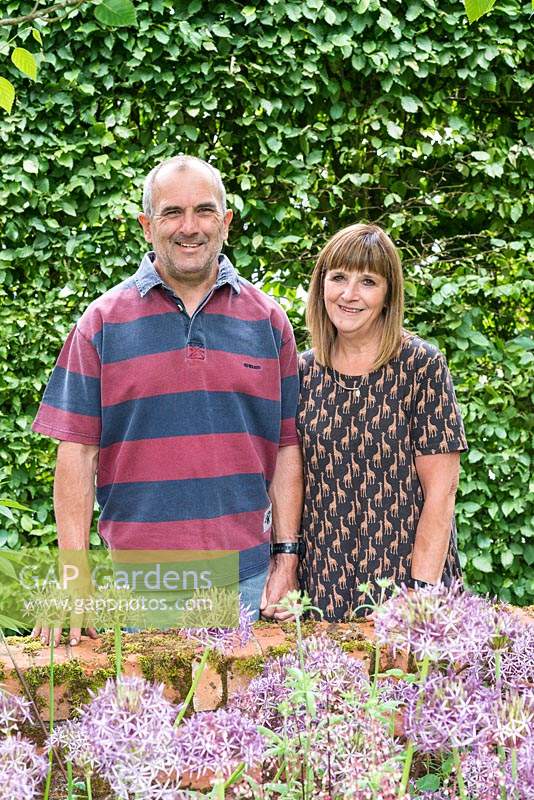 Garry and Alison Szafranski in their front garden in front of a hornbeam hedge and behind a bed of Allium cristophii.