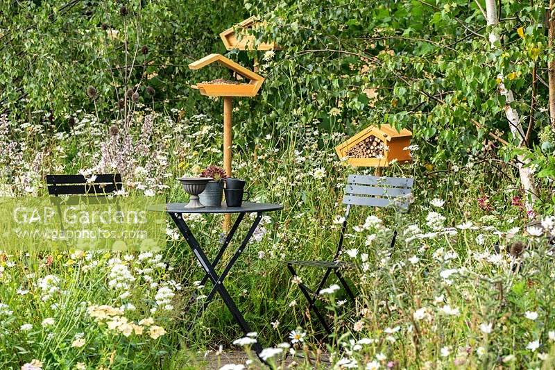 A seating area in a naturalistic wildlife friendly garden with wild and cottage garden flowers, providing a habitat for wildlife, birds, insects and bees. RHS Hampton Court Palace Garden Festival 2019.