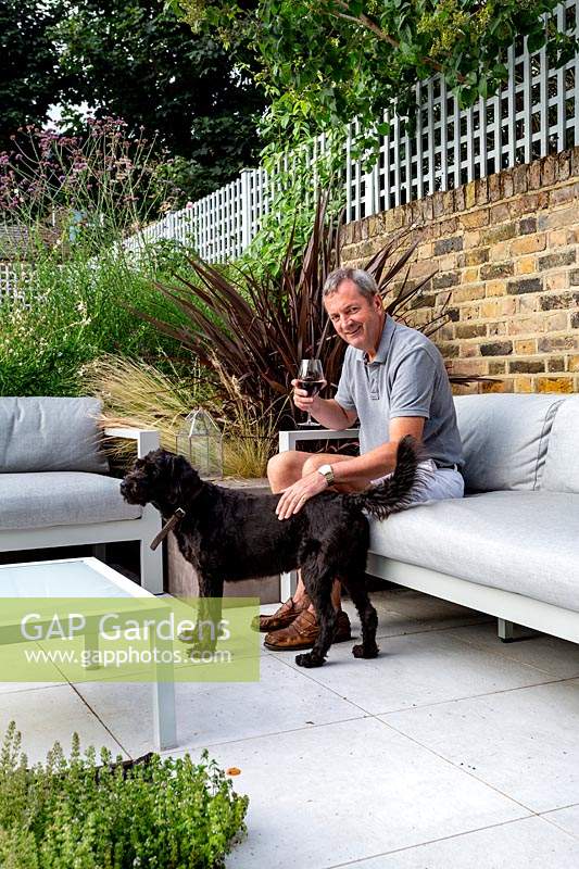 Man relaxing on sofa in outdoor room on patio, beside a pet dog