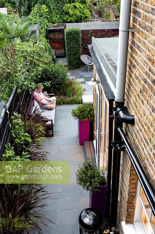 Jasper Martens, owner of small garden in West London sitting on garden sofa reading a book