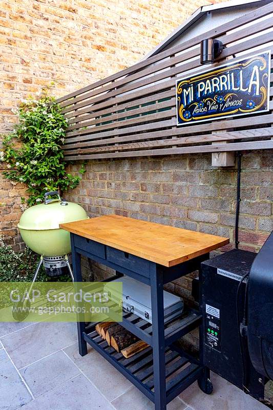 Dining patio area in small shade tolerant garden in London with a green theme. View across the patio towards barbecue.