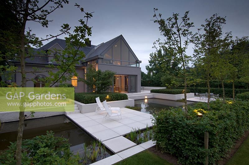 Modern house and garden, with paved areas surrounded by water. 