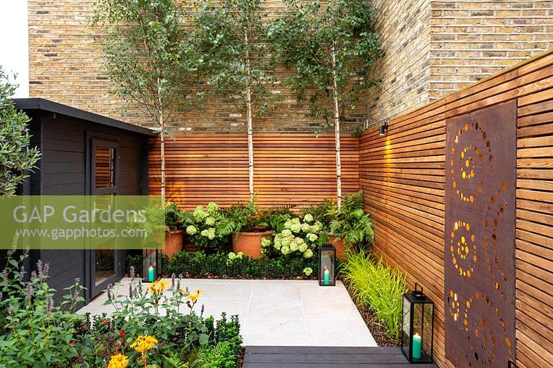 Small contemporary London garden with raised bed, bespoke garden seating with table and chairs and black wood garden room. 