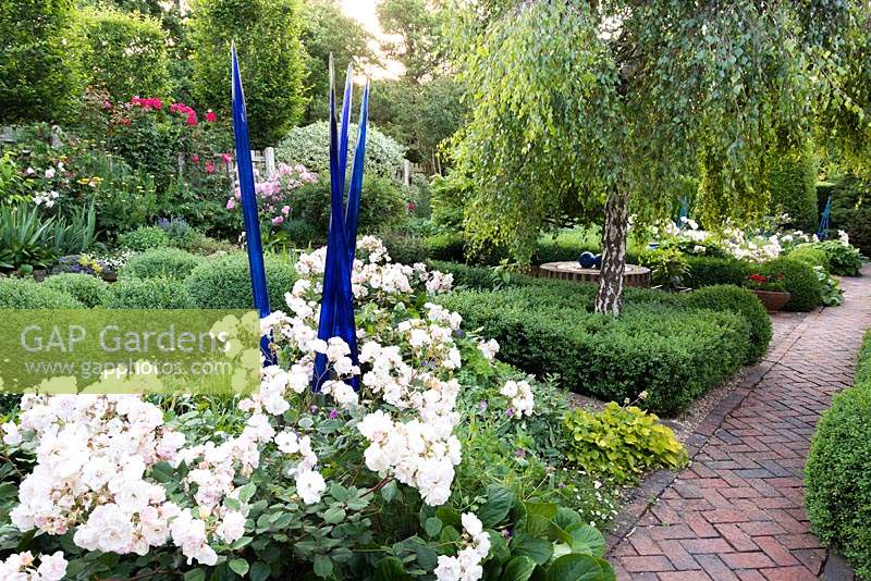 Rosa 'Penelope' - Rose - and blue glass sculpture with Betula - Weeping Silver Birch surrounded by clipped Buxus - Box. Herringbone brick path nearby 
