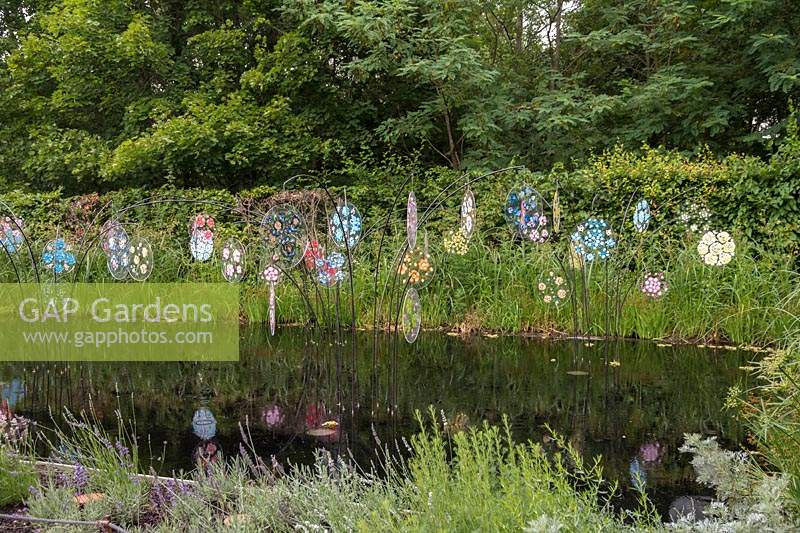 Elixir Floral,  Festival International des Jardins 2019, Domaine de Chaumont sur Loire, France. Glass flowers reflected in the water of a large pond.
