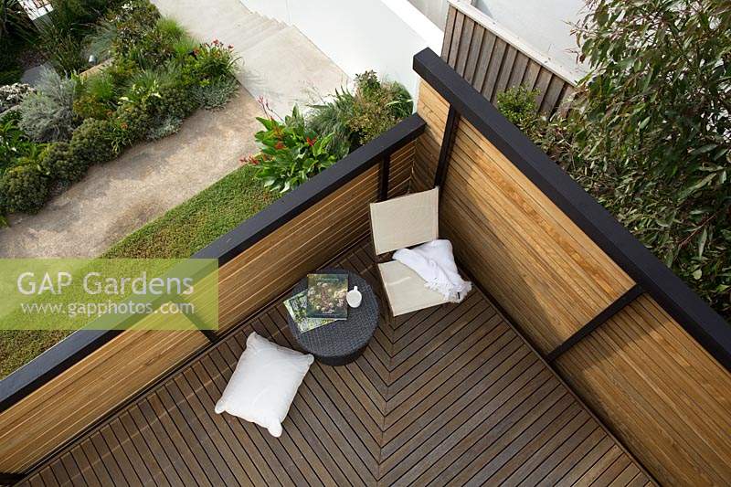 A birdseye view of a hardwood timber deck with an outdoor setting  of a table, chair and a cushion.