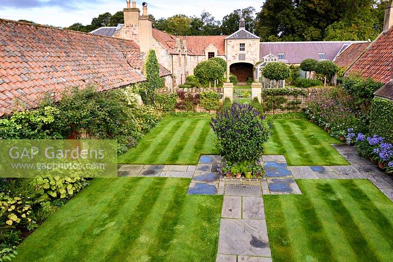The Lower Courtyard, laid out in a cruciform pattern with reclaimed flagstones, a central container planted with Salvia 'Amistad', walls lined with trained fruit trees and borders of eupatorium and agapanthus at Broadwoodside, Gifford, East Lothian in September