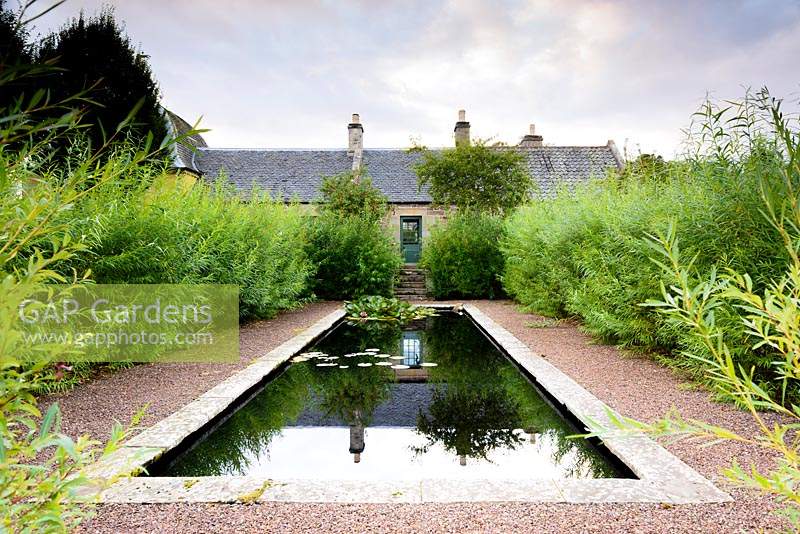 Formal pond surrounded by a willow hedge in the Walled Garden at Broadwoodside, Gifford, East Lothian in Scotland.