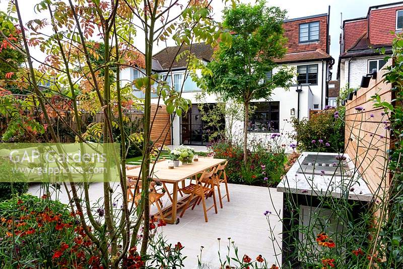 View of contemporary garden towards house in Wandsworth. With stone patio, seating and tables. With bespoke fitted barbecue.