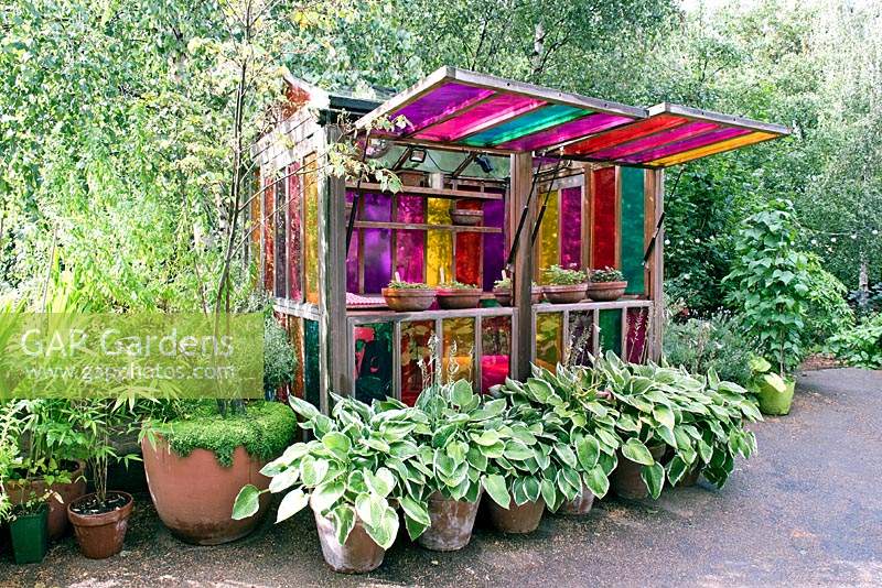 Colourful Greenhouse with coloured glass windows and Hostas in pots in front, Dalston Eastern Curve Garden, London Borough of Hackney.