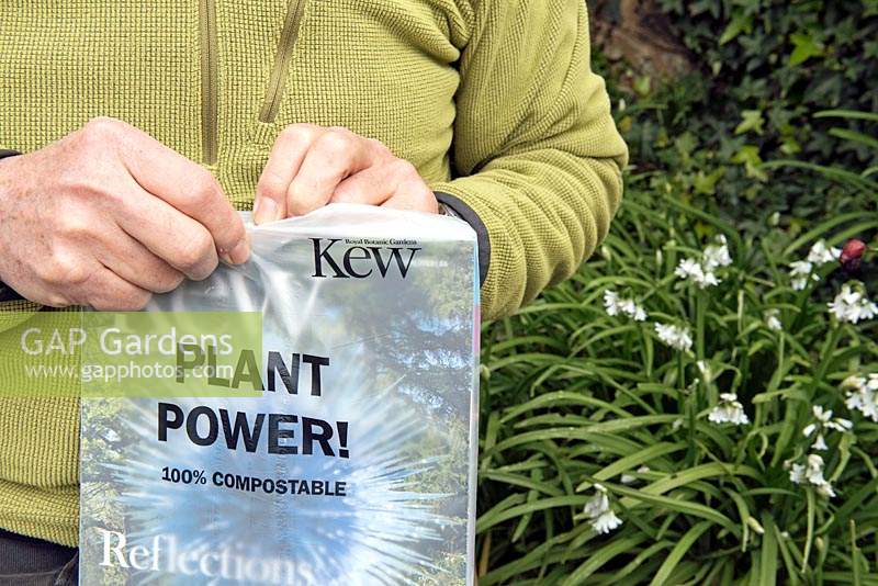 Man opening the new 100 percent compostable wrapping or packaging of Kew magazine in his garden.