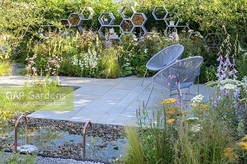 Seating area with two armchairs and rectangular water feature surrounded by aggregate and paving surface  - The Urban Pollinator Garden - RHS Hampton Court Palace Garden Festival, 2019  
Designer: Caitlin McLaughlin