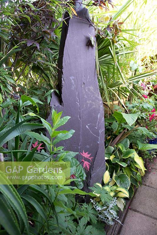 A slate monolith in a small town garden with tropical foliage plants â€‰