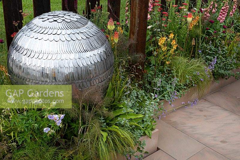 Round sculpture made from cutlery amongst the naturalistic planting in the 'Elements of Sheffield' garden at the RHS Chatsworth Flower Show 2019.