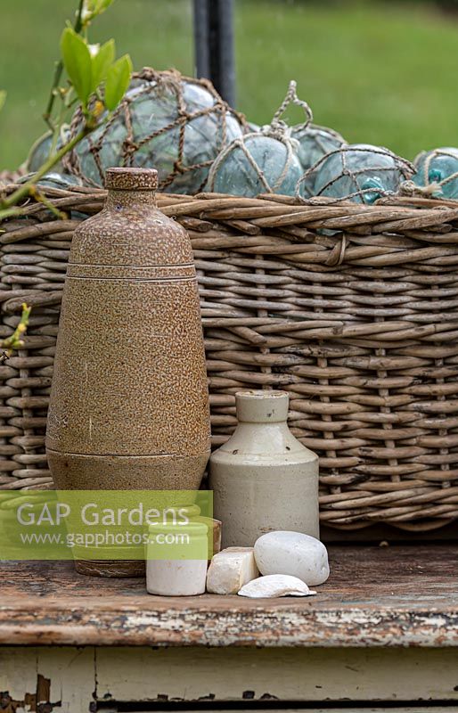 A collection of objects: earthenware bottles, a cane woven basket with glass fishing net floats, now used as decorative onraments