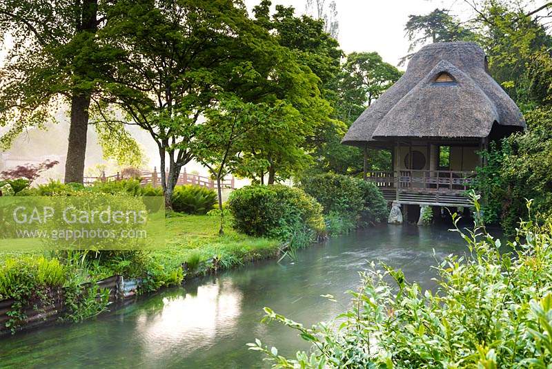 Japanese tea house straddling the River Avon running through the garden of Heale House, near Salisbury, Wiltshire in May with red Nikkon bridge beyond.
