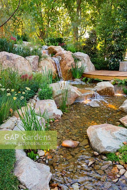A curved hardwood timber boardwalk leading to a rock garden with a waterfall, stream and rock garden.