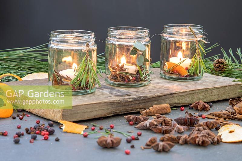 Scented candles made with spices, orange peel, pine and candles placed in jam jar on a wooden board