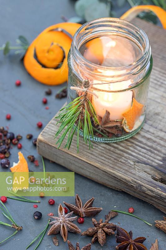 Scented candles made with spices, orange peel, pine and candles placed in jam jar on a wooden board