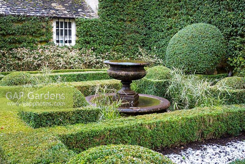A central water feature framed by clipped Buxus - Box - box, surrounded by Fuchsia magellanica 'Variegata' and walls trained with Pyracantha 