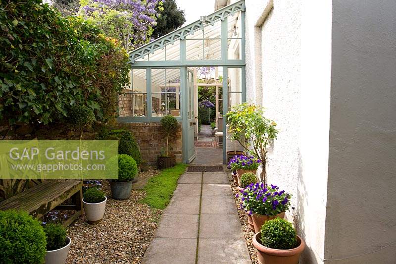 Lean-to conservatory against side of house, view along path lined with container plantings to door
