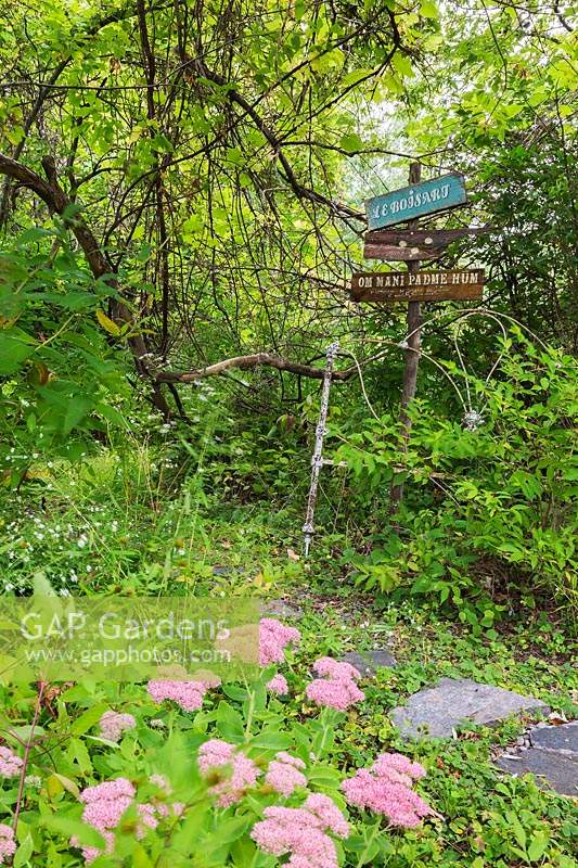 Signpost next to grey flagstone path through mixed deciduous tree forested area in residential front yard garden in late summer.