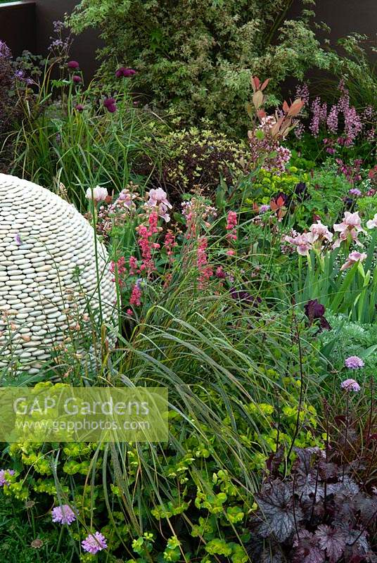 Herbaceous planting surrounding spherical feature made of pebbles in garden border - RHS Malvern Spring Festival 2014