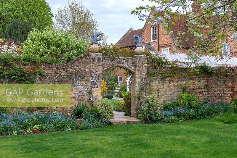 Ancient walls contain a walled garden, view through arch to period house beyond