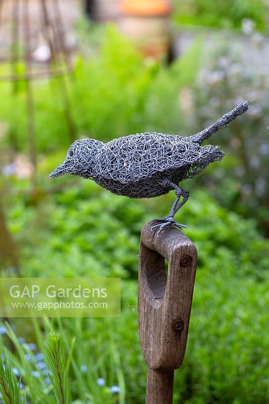 A wirework blackbird perched on a spade handle.