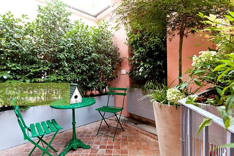 Tiled terrace with table and chairs, enclosed by troughs of shrubs fitted to fill gaps in walls  