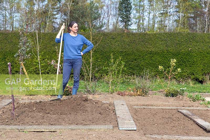 Woman having a break from soil preparation in new kitchen garden, resting on her rake
