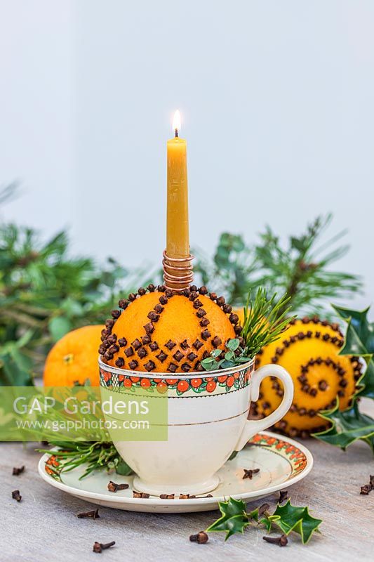 Orange studded with cloves in teacup holding a candle