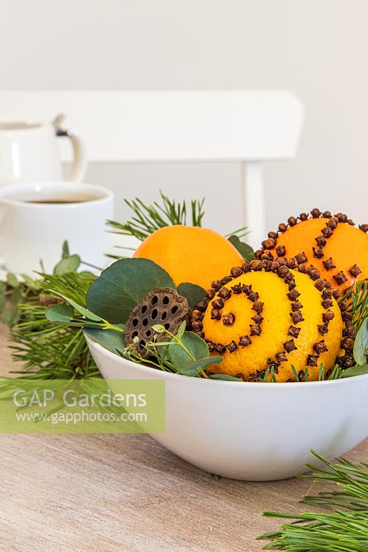 Table decoration with bowl full of clove-studded oranges with fresh and dried foliage