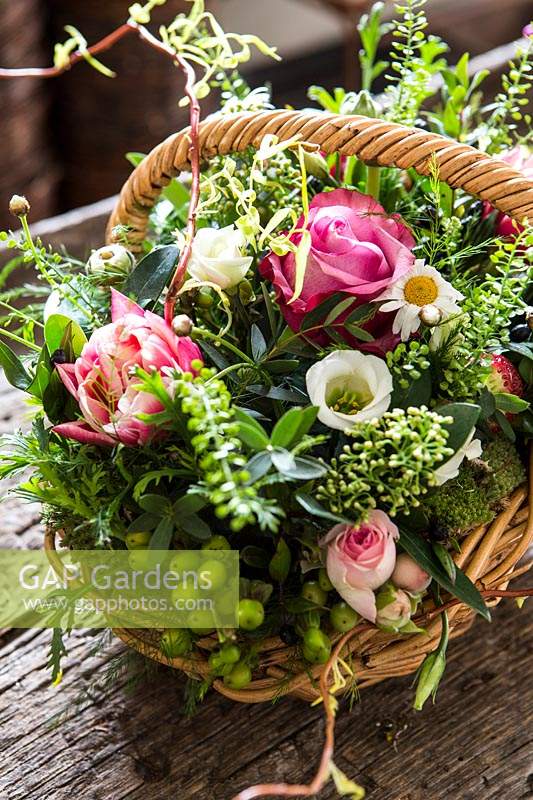 Floral arrangement in basket with roses, capsella busta pastoris, Hypericum and Eustoma. 