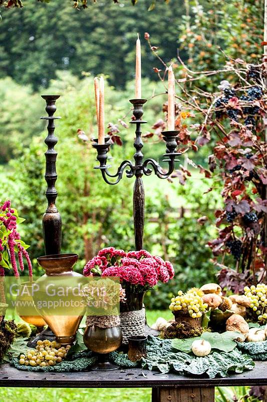 Autumn table decorated with hydrangeas, carnations, amaranth, grapes, savoy cabbage and mushrooms and candlesticks