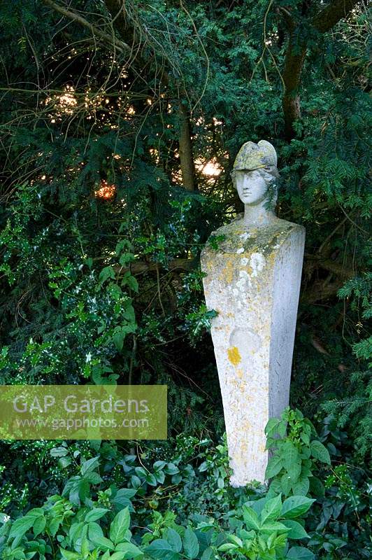Stone statue amongst evergreens Taxus - Yew - and Ilex - Holly