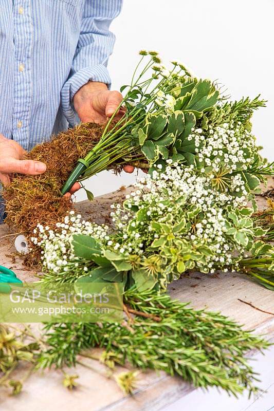 Woman fixing Chrysanthemum in floral water tube to moss wreath form.
