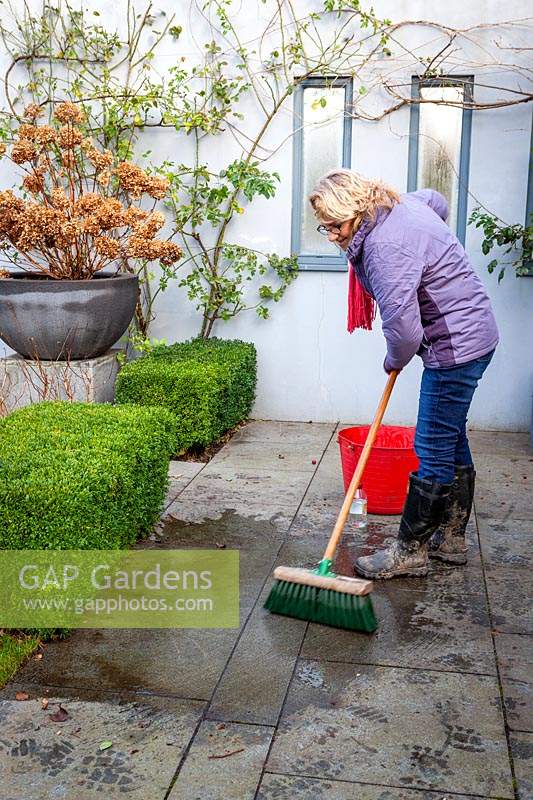 Cleaning a patio using a long-handled brush, water and vinegar