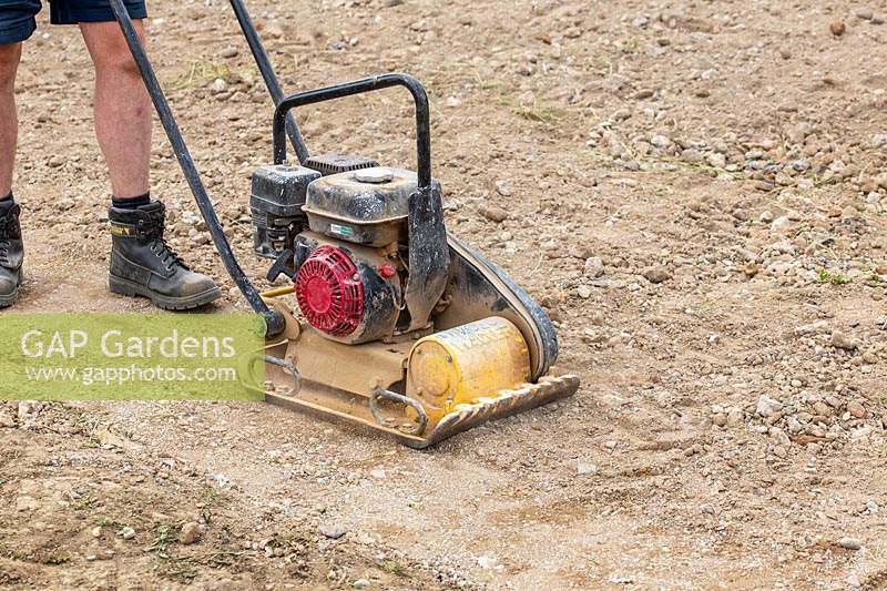 Man using petrol driven wacker plate to compact base for patio