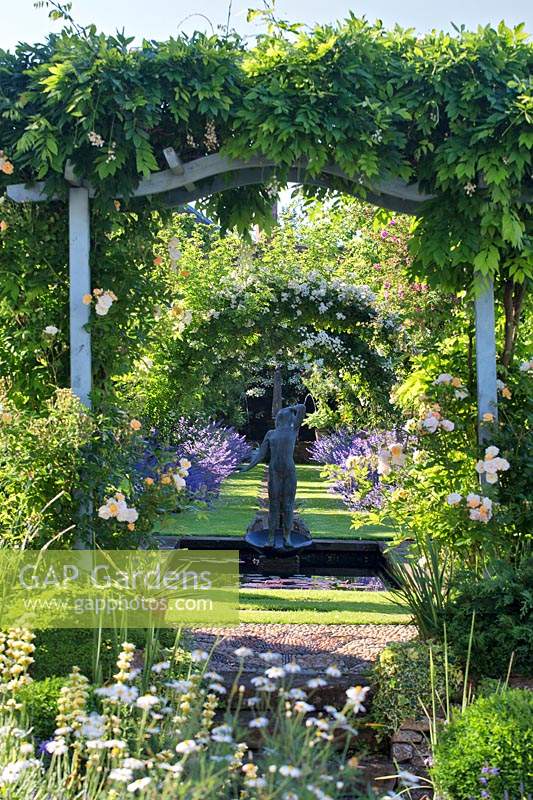 View through a Wisteria-covered pergola to a rectangular pond with sculpture