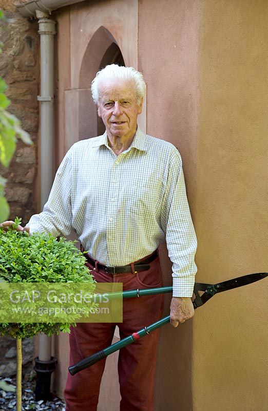 Man holding long-handled shears, standing by topiary