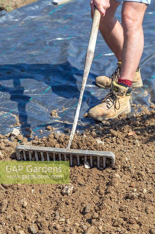 Man using a rake to level out sand, hardcore and gravel mix ontop of membrane