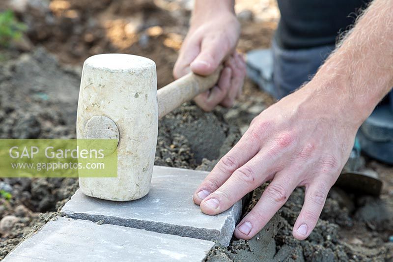 Man using rubber mallet to  level freshly laid sandstone setts